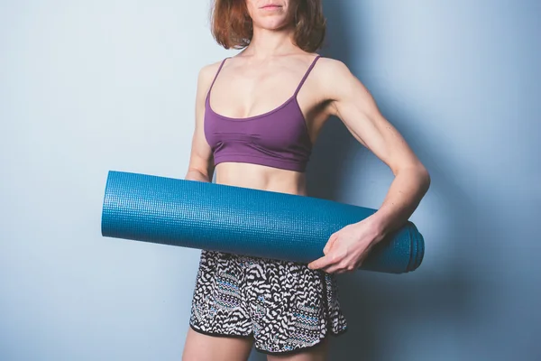 Mujer joven atlética sosteniendo una esterilla de yoga — Foto de Stock