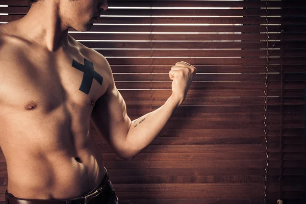 Young man flexing his muscles by window — Stock Photo, Image