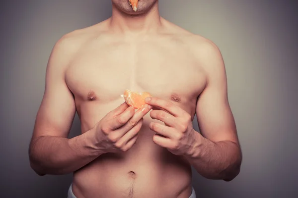 Мужчина в спортивной рубашке чистит апельсин — стоковое фото