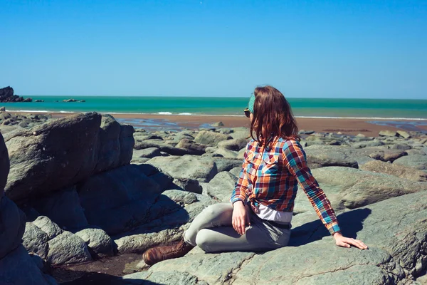 Jovem mulher sentada em uma praia rochosa — Fotografia de Stock