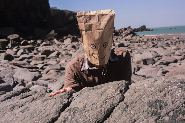 Bărbat cu pungă de hârtie deasupra capului pe plajă — Fotografie, imagine de stoc