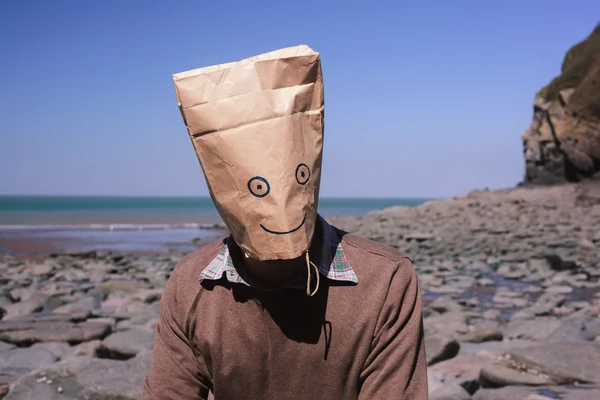 Человек с бумажным мешком на голове на пляже — стоковое фото