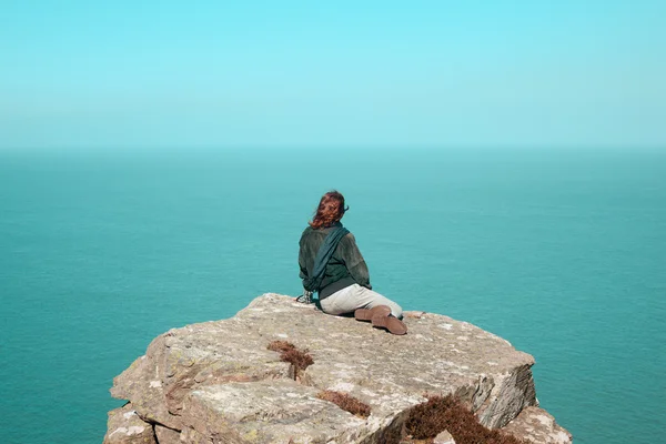 Młoda kobieta siedząca na klifie nad morzem — Zdjęcie stockowe