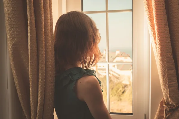 Mujer joven en vestido mirando por la ventana — Foto de Stock