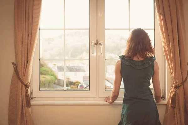Junge Frau im Kleid schaut aus dem Fenster — Stockfoto