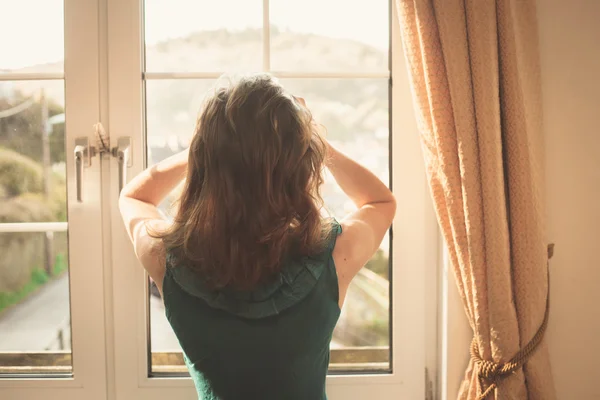 Ung kvinna i klänning som tittar ut genom fönstret — Stockfoto