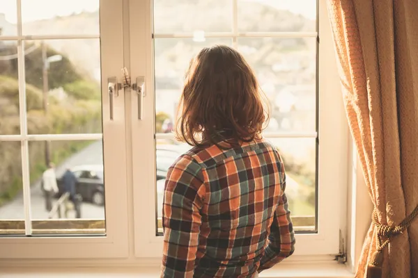 Ung kvinna som tittar ut genom fönstret — Stockfoto