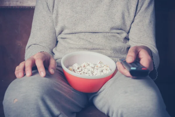 Młody człowiek, oglądanie telewizji i jedzenie popcornu — Zdjęcie stockowe
