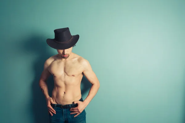 Sem camisa cowboy golpeando um pose por azul parede — Fotografia de Stock