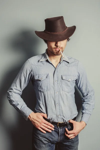 Cowboy em pé junto a uma parede azul fumando cigarro — Fotografia de Stock