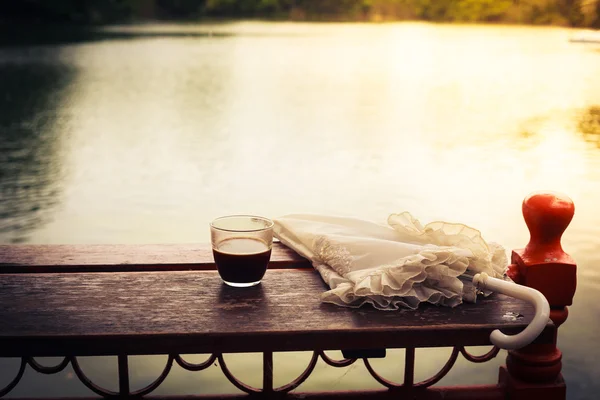 Koffie en paraplu op tafel aan het meer — Stockfoto