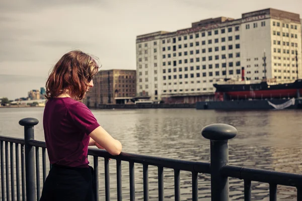 Young woman relaxing by river and looking across at buildings — Stock Photo, Image