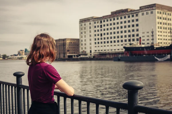 Young woman relaxing by river and looking across at buildings — Stock Photo, Image