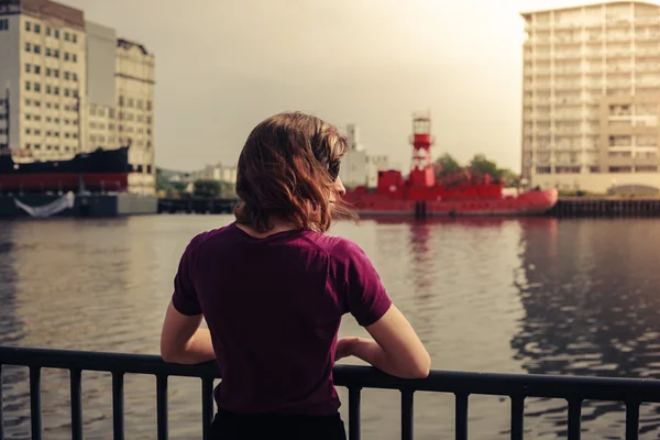 Mujer joven relajándose por el río y mirando a través de los edificios — Foto de Stock