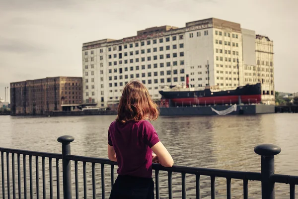 Giovane donna rilassante sul fiume e guardando attraverso gli edifici — Foto Stock
