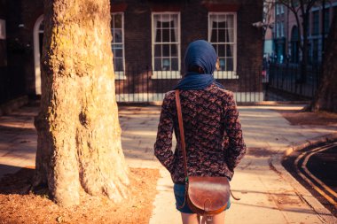 güneşli bir günde şehirde yürüyen genç bir kadın