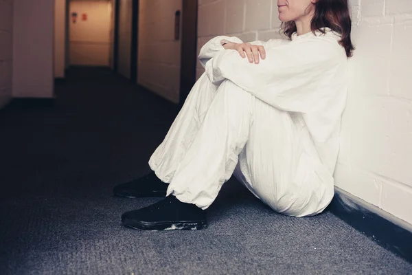 Upset woman in boiler suit sitting in corridor