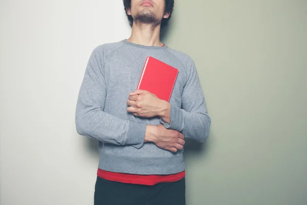 Giovane uomo con libro rosso contro lo sfondo di colore split — Foto Stock
