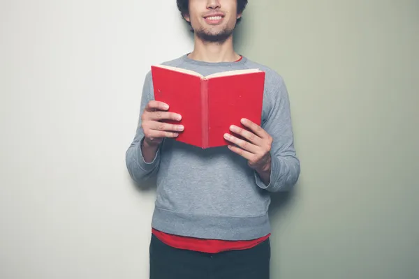 Ung man med röd bok mot split färgad bakgrund — Stockfoto