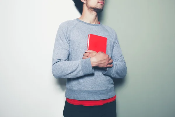 Молодой человек с красной книгой на раскрашенном фоне — стоковое фото