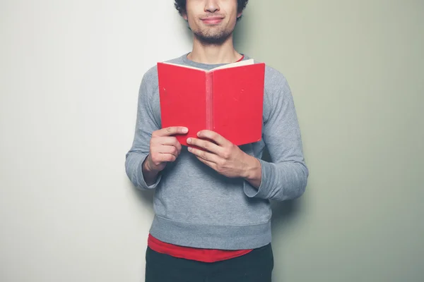 Νεαρός άνδρας με το κόκκινο βιβλίο κατά διαίρεση έγχρωμο φόντο — Φωτογραφία Αρχείου