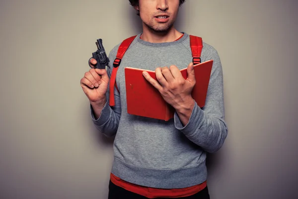 Студент с пистолетом и книгой — стоковое фото