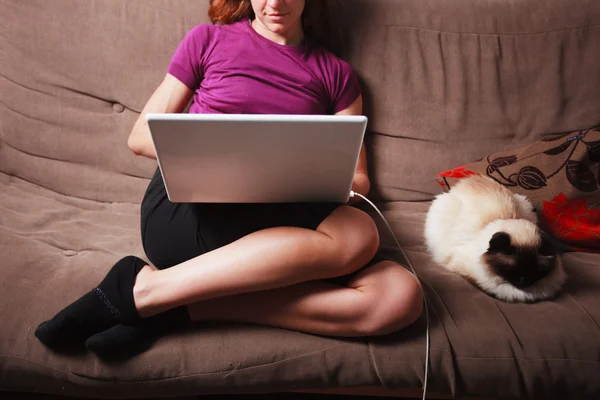 Mujer joven usando computadora portátil con gato al lado de ella — Foto de Stock