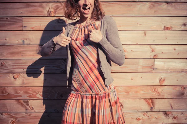 Young woman giving thumbs up outside wooden cabin — Stock Photo, Image