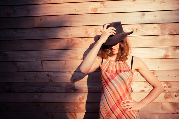 Young woman wearing cowboy hat by a cabin — Stock Photo, Image