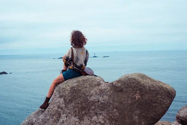 Deniz kenarında bir kayaya oturan genç kadın — Stok fotoğraf