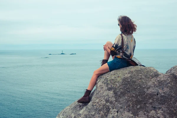 Jovem mulher sentada em uma rocha junto ao mar — Fotografia de Stock