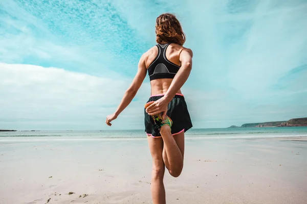 Atletische jonge vrouw uitrekken op het strand — Stockfoto