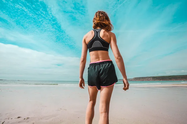 Sportovní mladá žena stojící na pláži — Stock fotografie