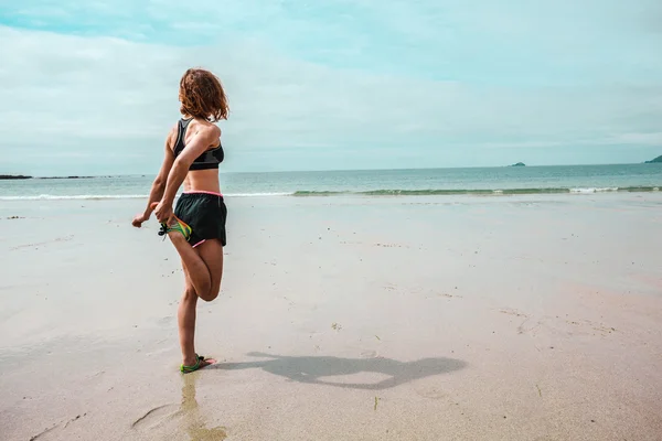 Jonge vrouw die zich uitstrekt haar been op strand — Stockfoto