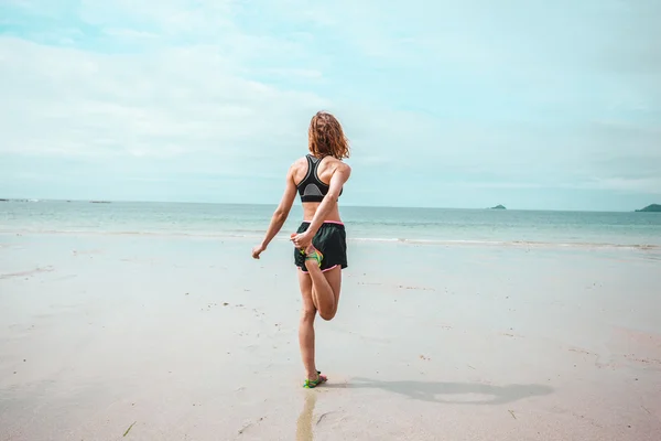 Ung kvinna stretching hennes ben på stranden — Stockfoto