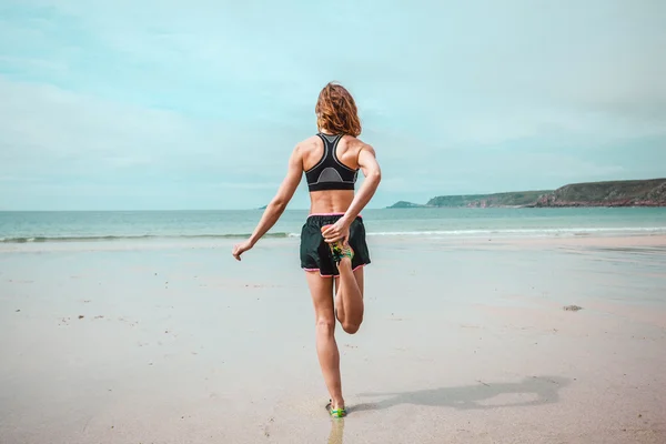 Jonge vrouw die zich uitstrekt haar been op strand — Stockfoto