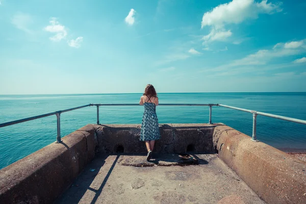 Mujer joven de pie en un muelle junto al océano —  Fotos de Stock