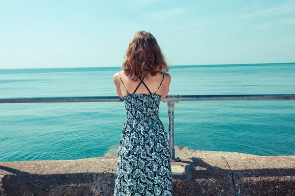 Mujer joven de pie en un muelle junto al océano — Foto de Stock