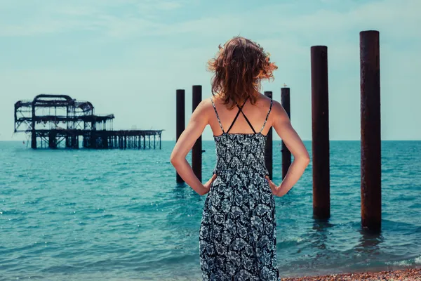 Jonge vrouw permanent door de oceaan met oude pier — Stockfoto