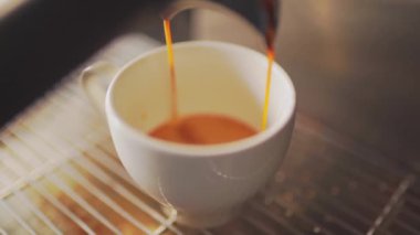 4k, espresso kahve makinesinden beyaz bir fincana dökülüyor, ağır çekimde.