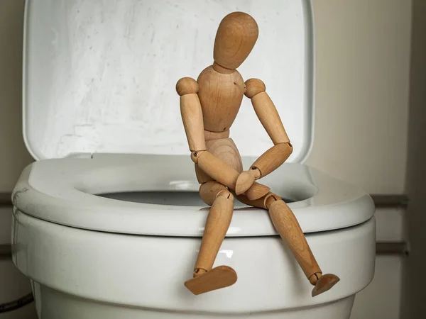 Wooden figure of a man sitting on the toilet in the toilet, health problems, constipation, diarrhea, abdominal pain