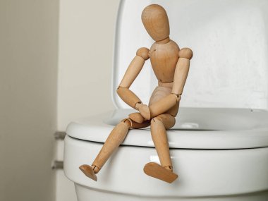 Tuvalette oturup karnını tutan bir insan figürü. Kabızlık, hemoroit, acı sorunu.