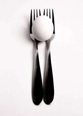 Metal çatalların üzerinde tavuk yumurtası, beyaz arka planda izole edilmiş kaşıklar. İki çatalın üzerine yerleştirilmiş bir yumurta, kaşıklar. Yumurtaların diyetten yemek tariflerine kadar pek çok kullanım alanı vardır..