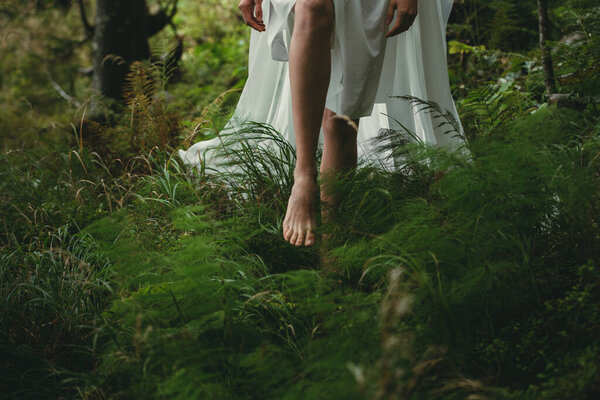 Young girl goes barefoot in a white dress on the green grass in the woods on a sunny day, front view the average plan