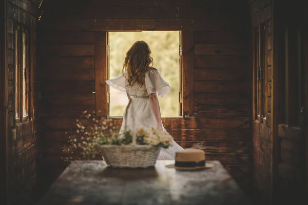Pencerenin yanındaki elbiseli kız ve bir sepet çiçek. — Stok fotoğraf
