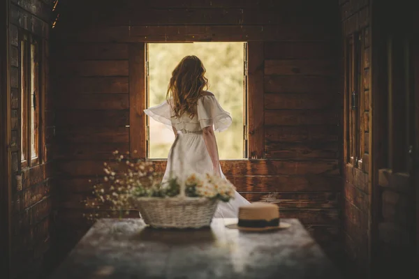 Flicka i klänning vid fönstret och en korg med blommor — Stockfoto