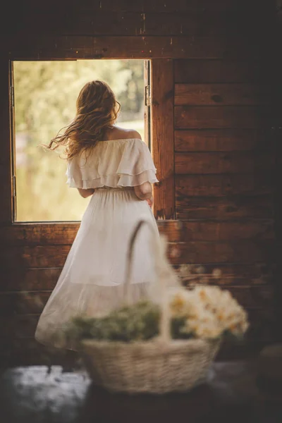 Flicka i klänning vid fönstret och en korg med blommor — Stockfoto
