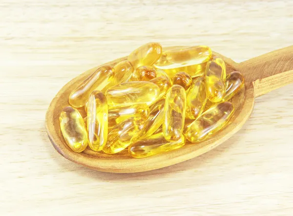 Fish oil capsules on wooden spoon — Stock Photo, Image