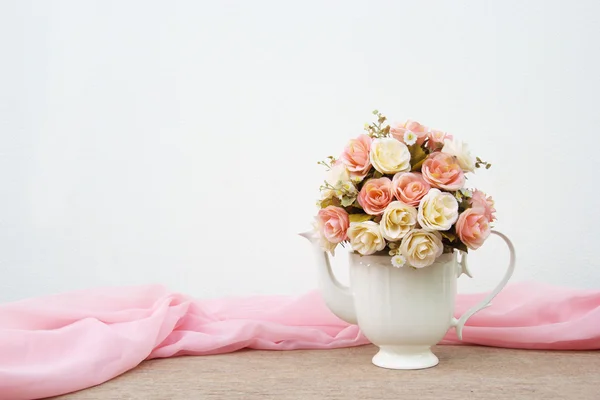 Rosenstrauß in weißem Krug auf Holztisch und rosa Stoffhintergrund — Stockfoto