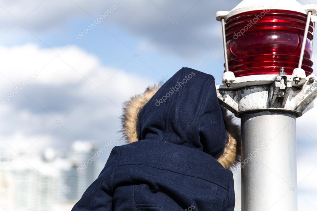 The back of child in dark blue coat leaning against the red beacon